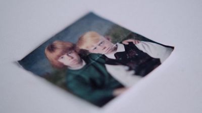 Film still from 'Stormy Luke' (2023) by Jon Beaton. Lying on a white surface is a small copy of a school photo of two brothers looking grumpy.